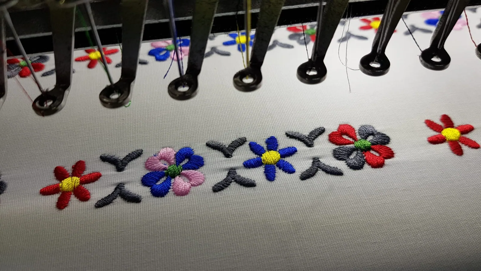Vyšívací stroj pri vyšívaní farebných kvetov na biely textil