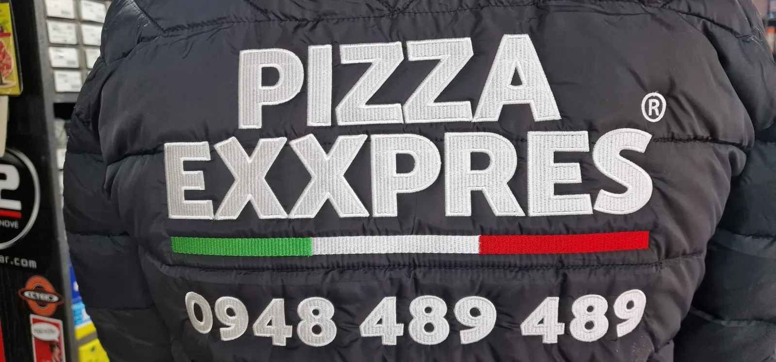 Vyšívané logo pizzerie na chrbte čiernej bundy