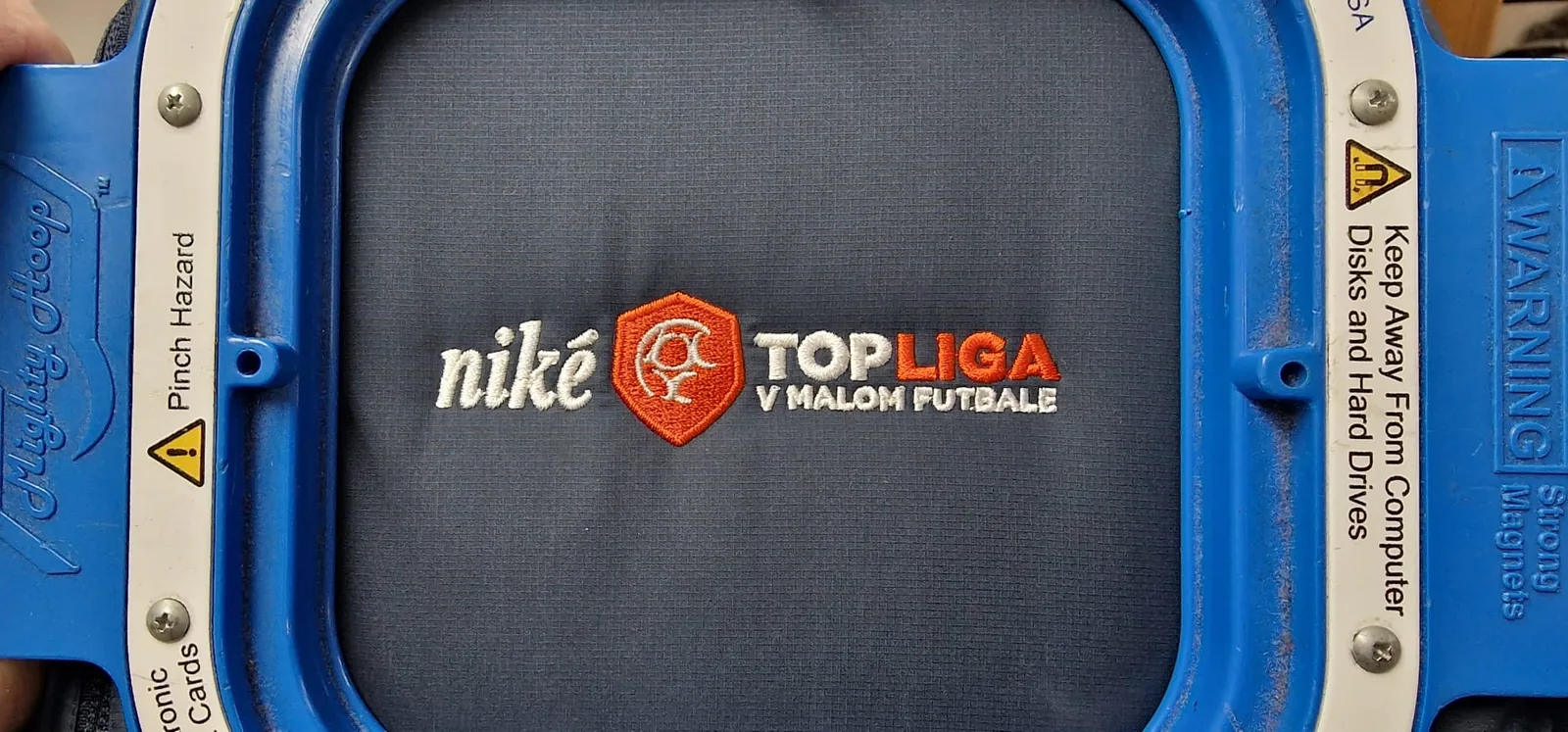 Logo futbalovej súťaže vyšité na tmavej látke vo vyšívacom ráme