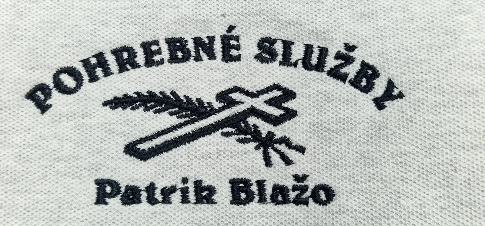 Vyšívané firemné logo s krížom a vetvičkou na svetlej polokošeli
