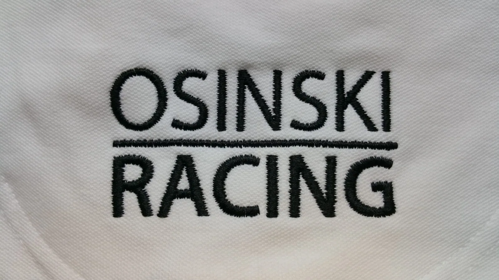 Čierne vyšité logo pretekárskeho tímu na bielej polokošeli