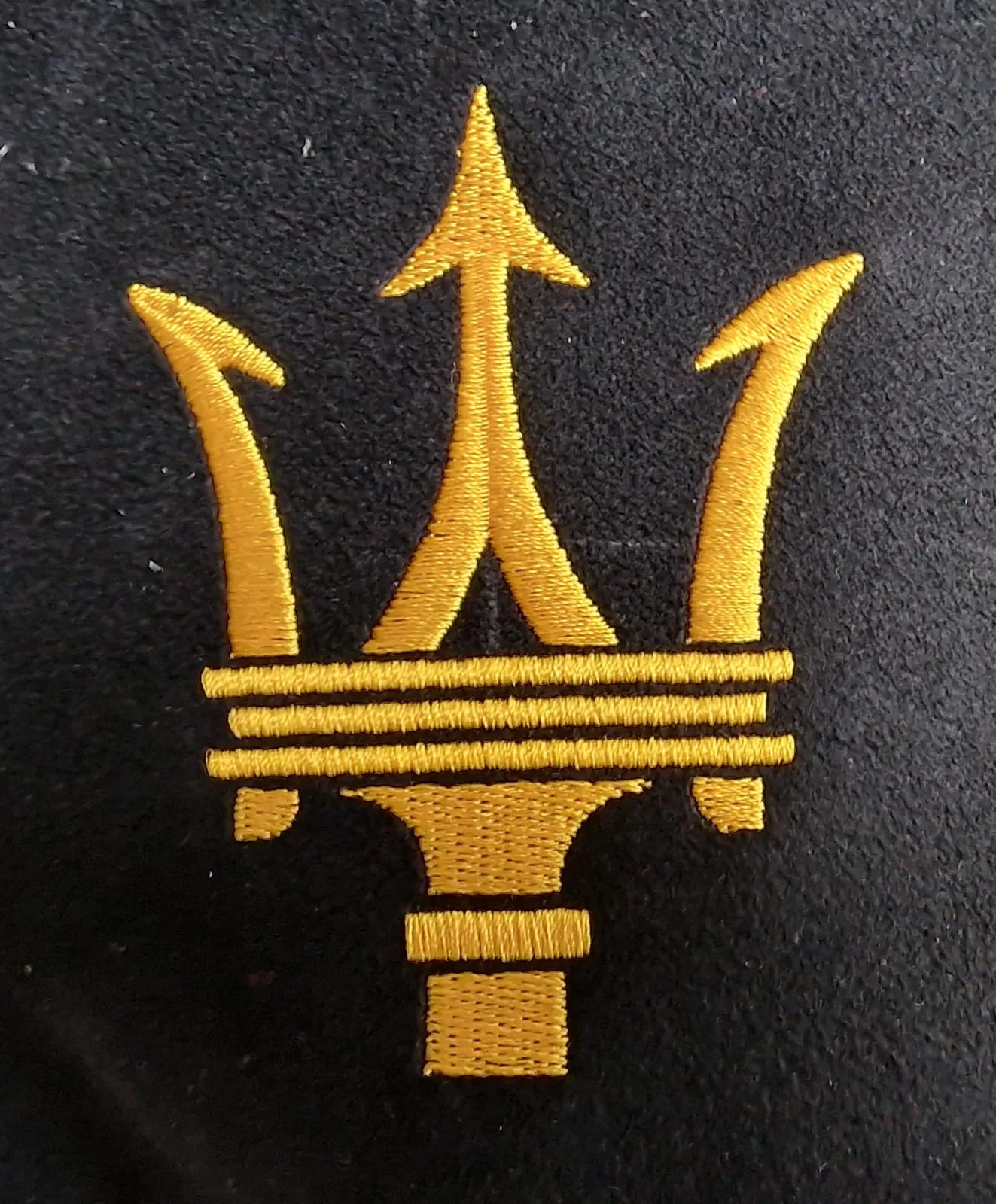 Zlatý vyšitý trojzubec na čiernom textile