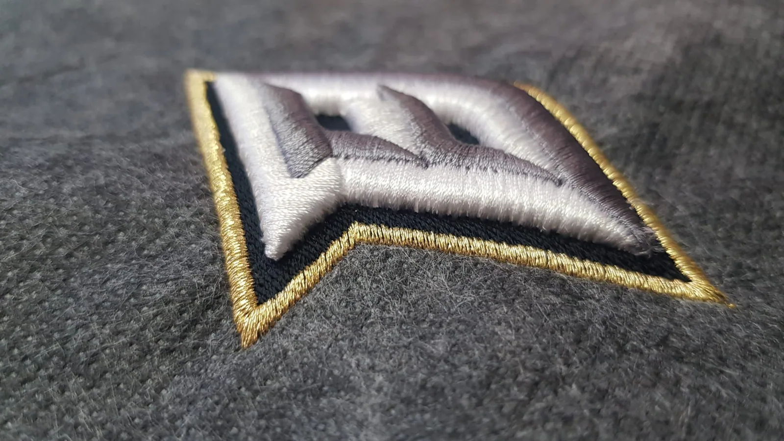 Detail 3D výšivky loga so zlatým lemom na šiltovke