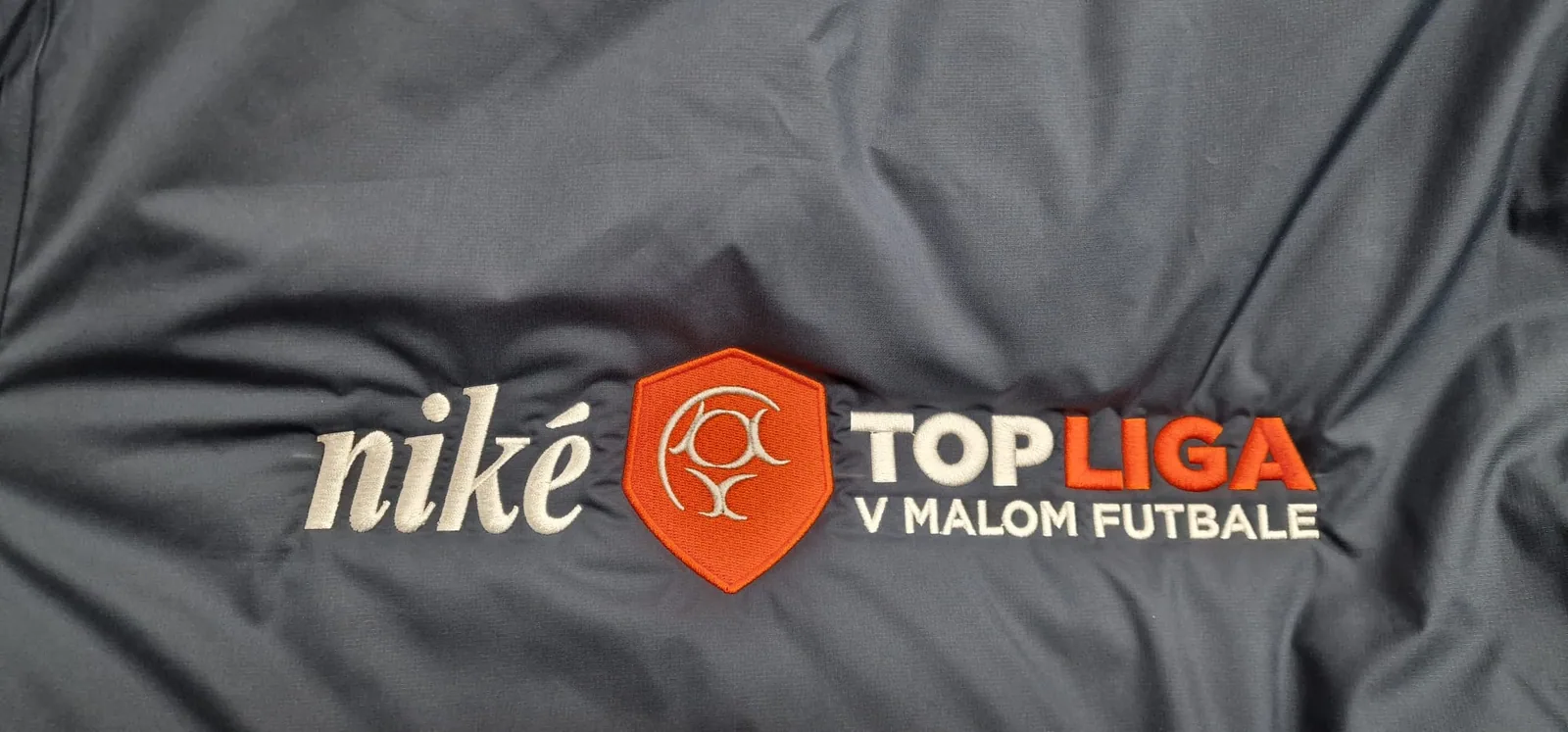 Farebné vyšité logo futbalovej súťaže na čiernej bunde