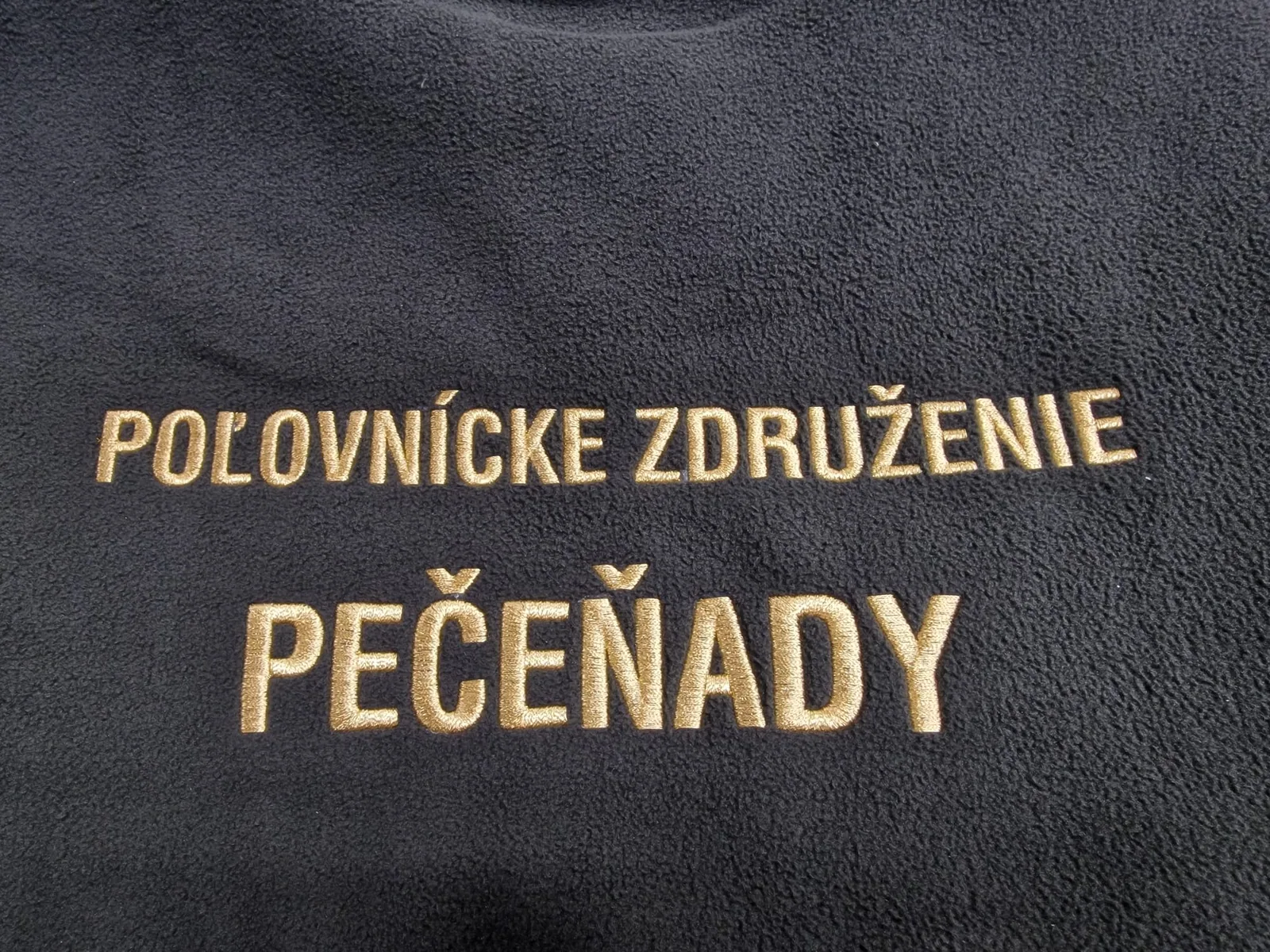 Zlatý vyšitý nápis poľovníckeho združenia na tmavej mikine