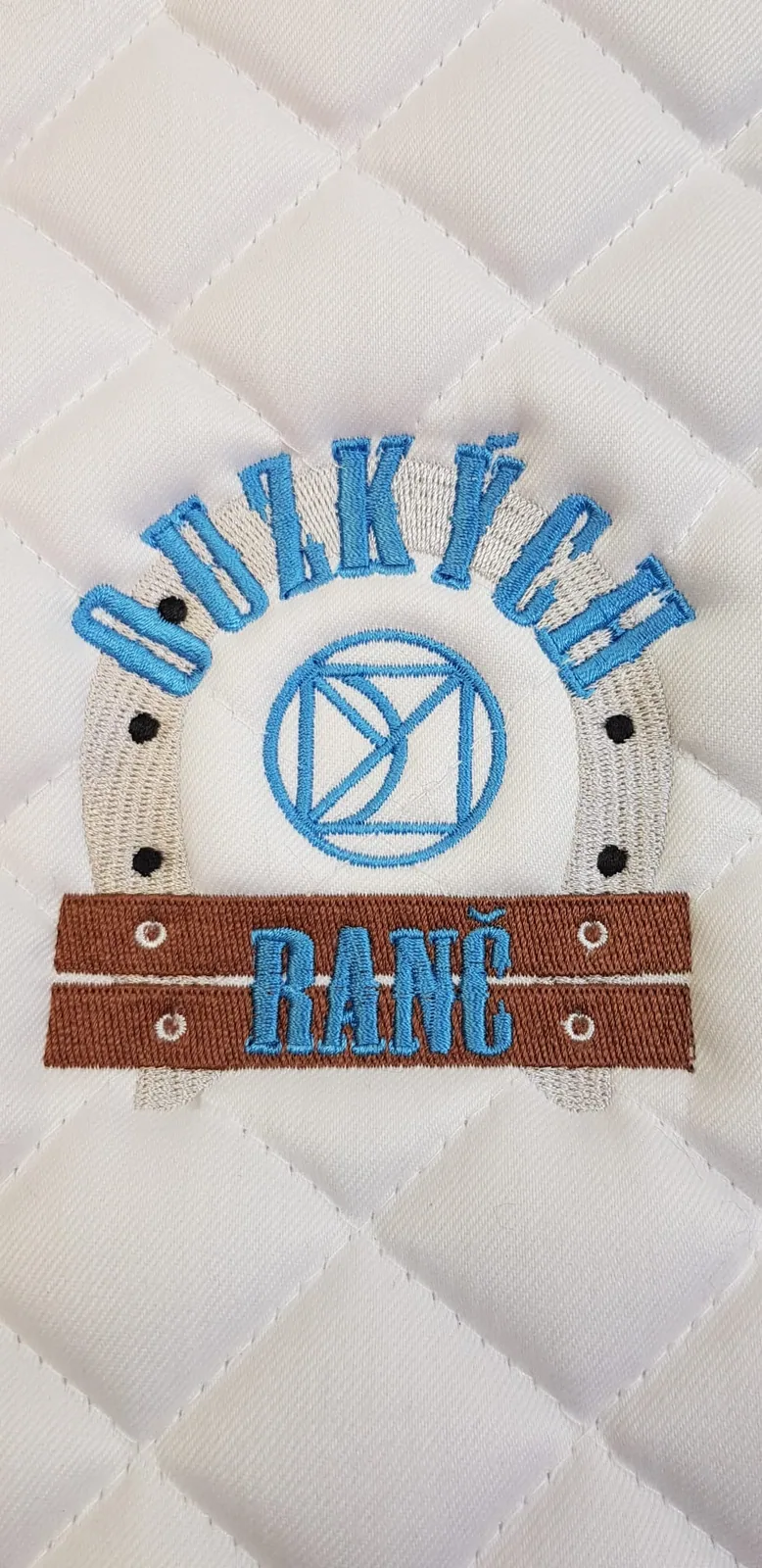 Vyšité logo ranča na bielej podsedlovej deke