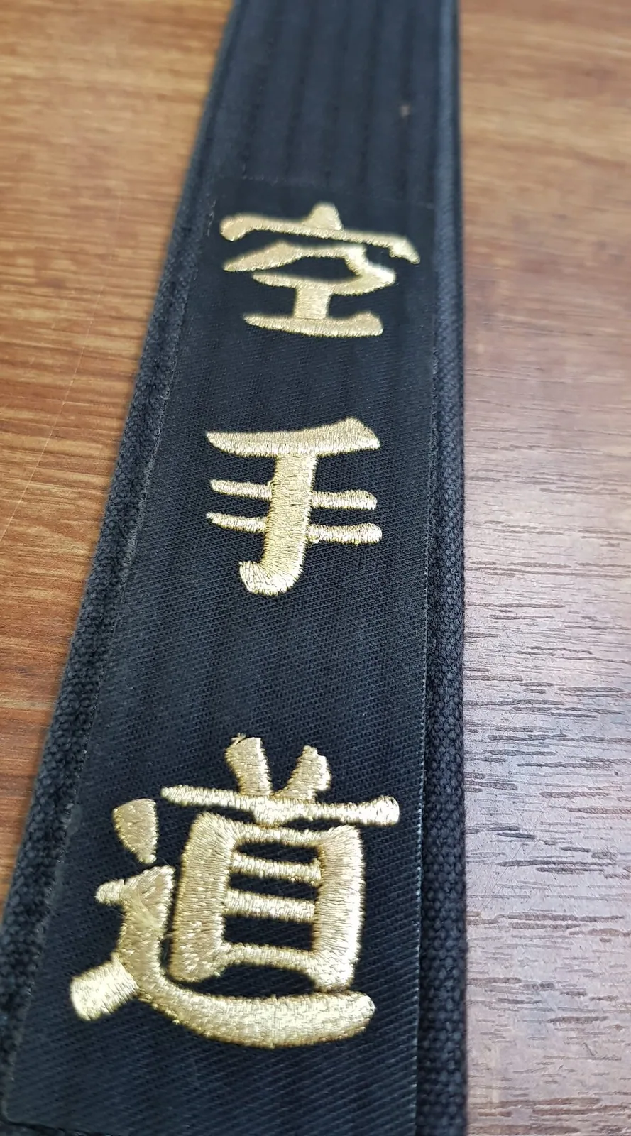 Zlatá výšivka japonských znakov na čiernom karate opasku