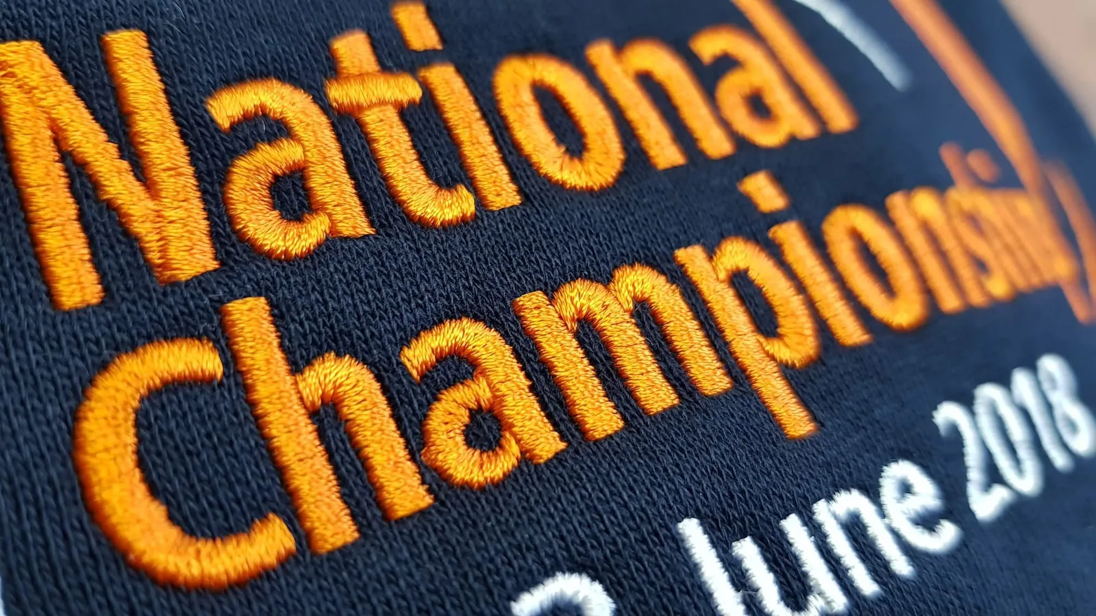 Detail oranžového vyšitého nápisu na tmavom textile