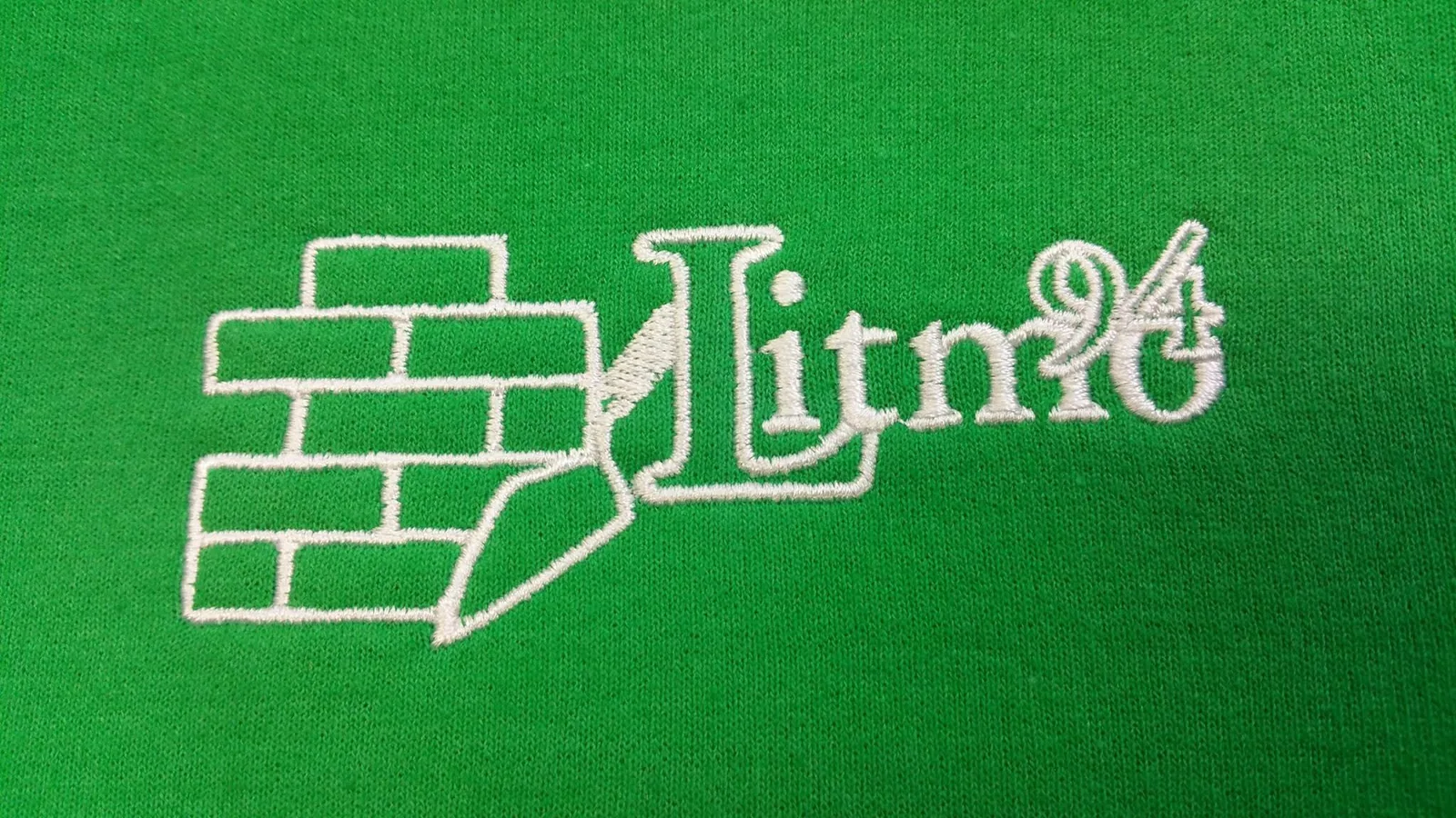 Biele vyšité logo s tehlami na zelenom textile