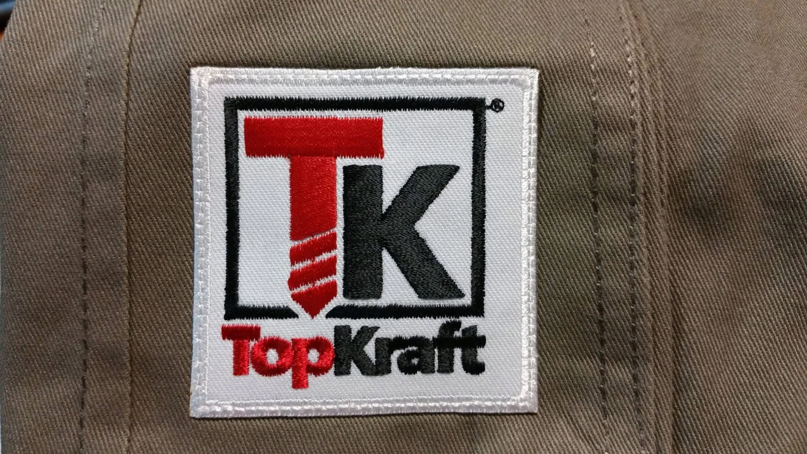 Štvorcová vyšívaná nášivka s logom na hnedom textile
