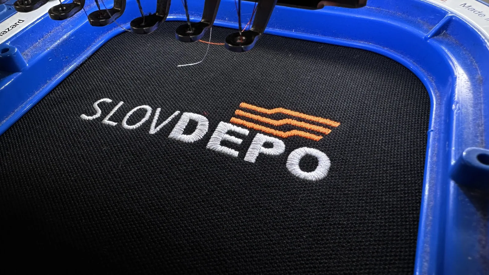 Vyšité firemné logo na čiernom textile vo vyšívacom ráme