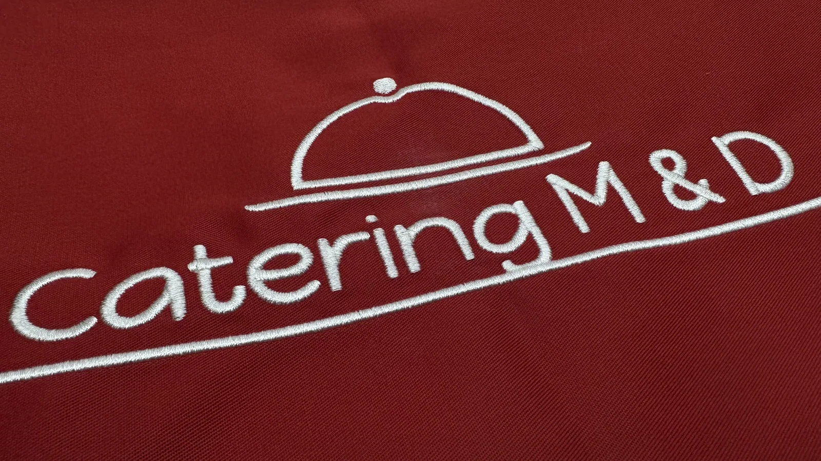Biele vyšité logo cateringu na červenom textile