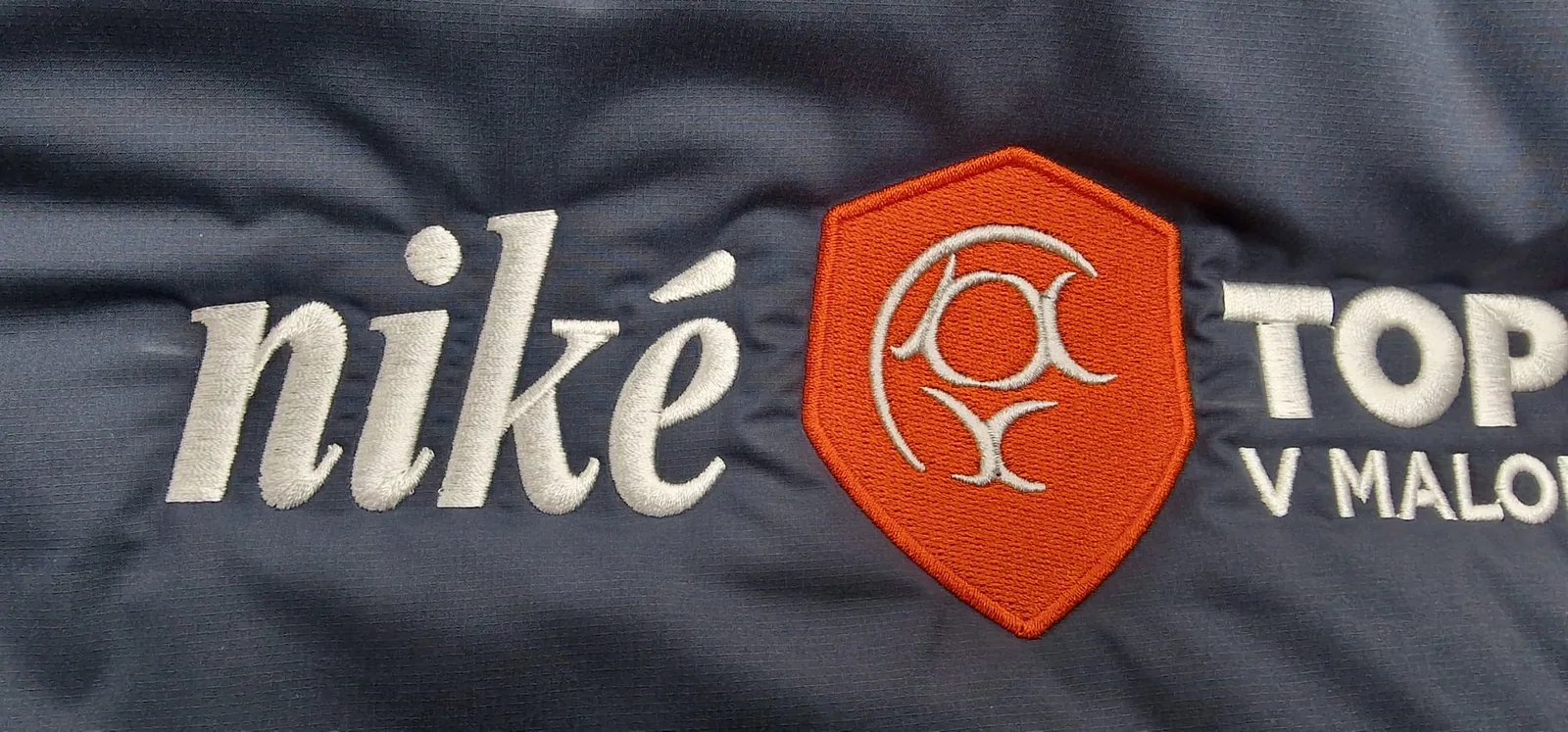 Detail bieleho a oranžového vyšitého loga na tmavej bunde