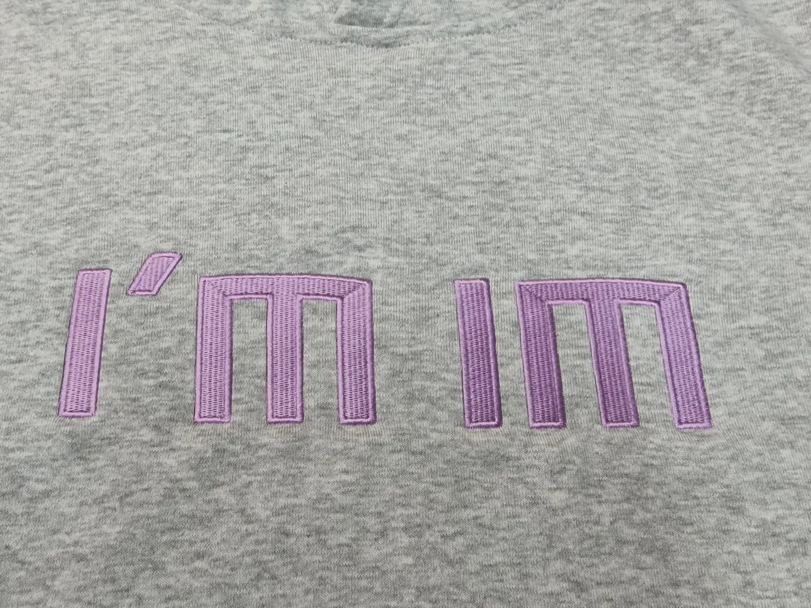 Fialový vyšitý nápis na sivej mikine
