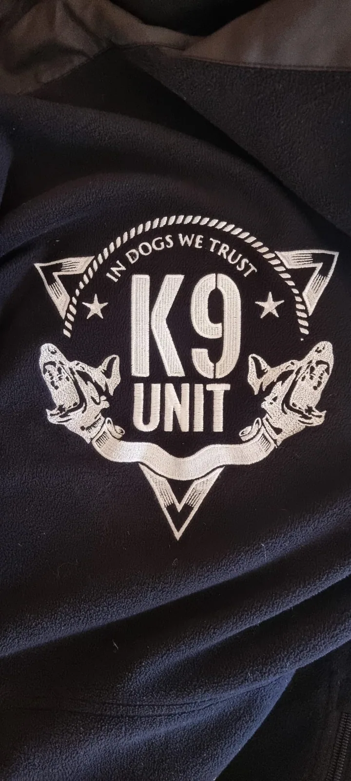 Biele vyšité logo kynologickej jednotky na čiernej bunde